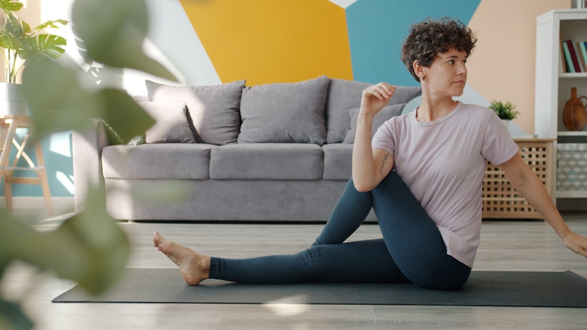 Beautiful lady exercising at home doing yoga stretching body caring for health, girl is wearing trendy and comfortable clothing. People and active lifestyle concept.